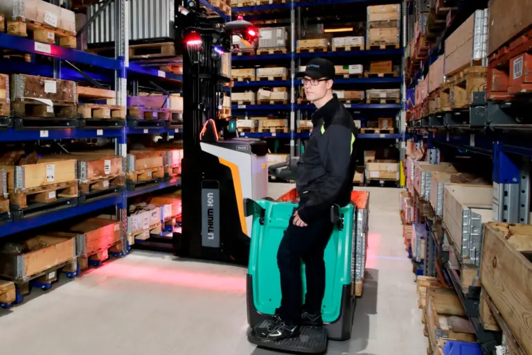 Medarbejder i Logisnext Denmark-kasket kører palleløfter forbi Rocla AGV-truck med sikkerhedsprojektion